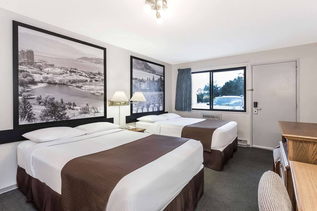 A hotel room with two beds, a desk, a chair, and large framed pictures on the wall.