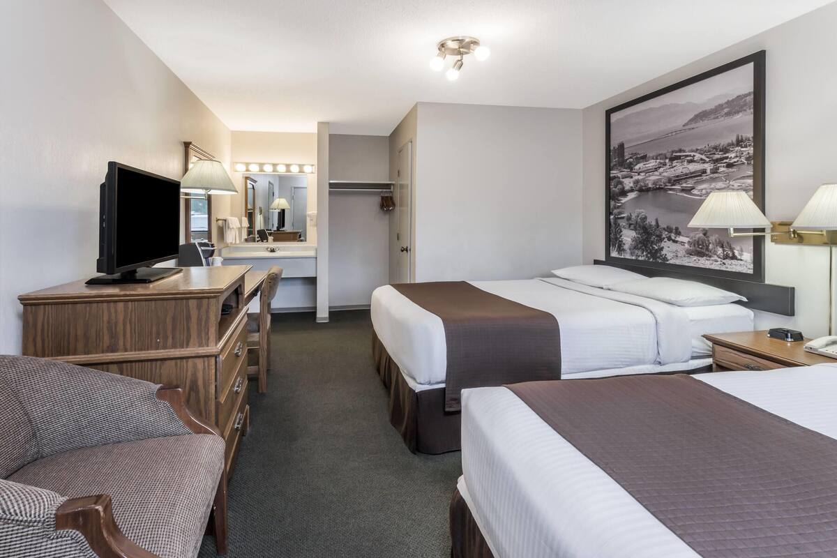 A hotel room with a desk, two beds, a TV, a mirror, and a large framed picture on the wall.