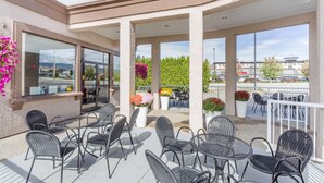 Een terras buiten met rieten tafels en stoelen, potplanten en uitzicht op de stadslijn.