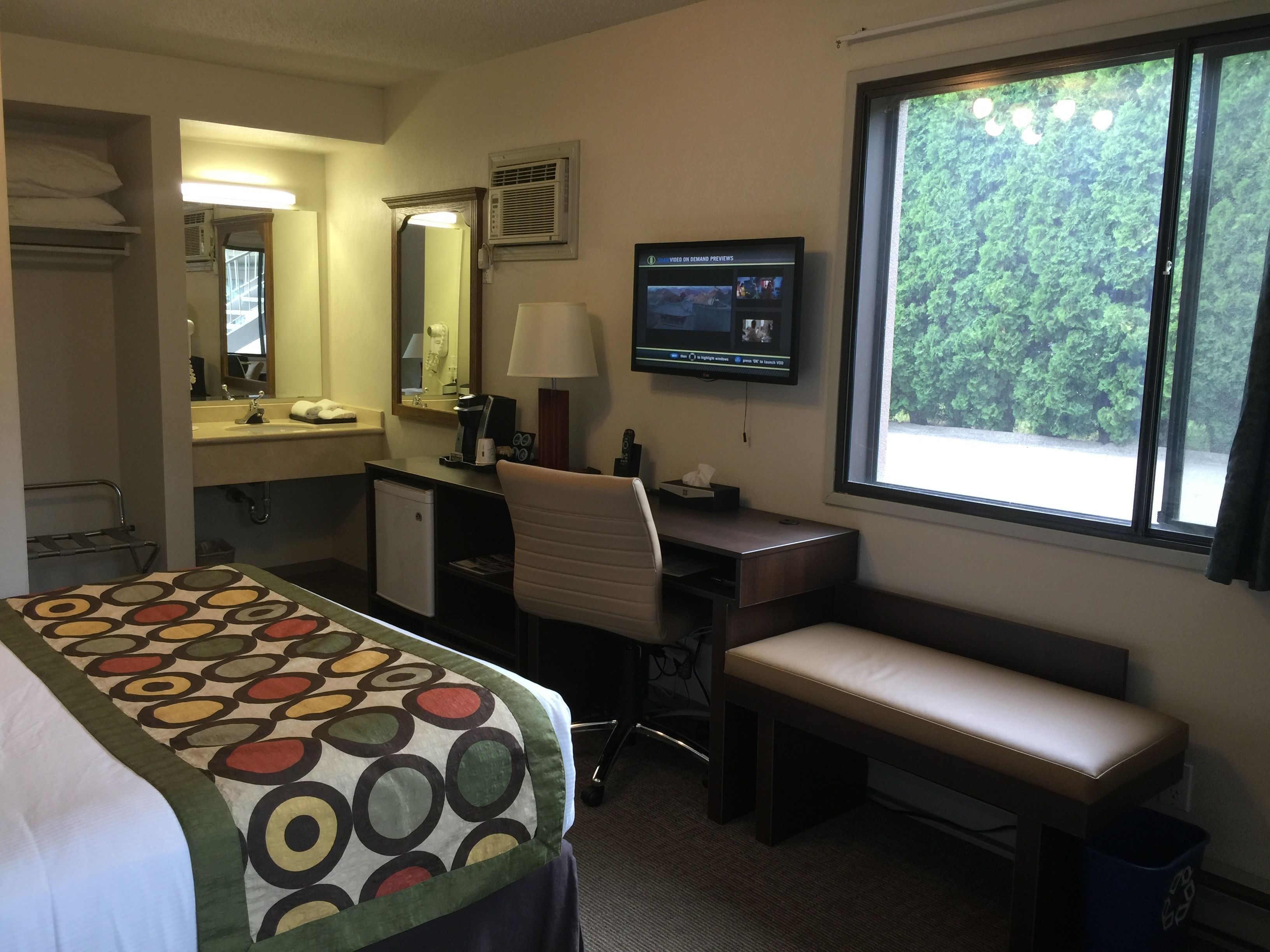 A hotel room with a bed, desk, chair, and a television.