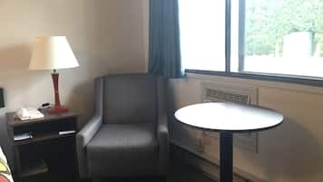 Habitació d'hotel amb una butaca gris, una taula petita, una làmpada, un telèfon i una finestra amb vista a vegetació.