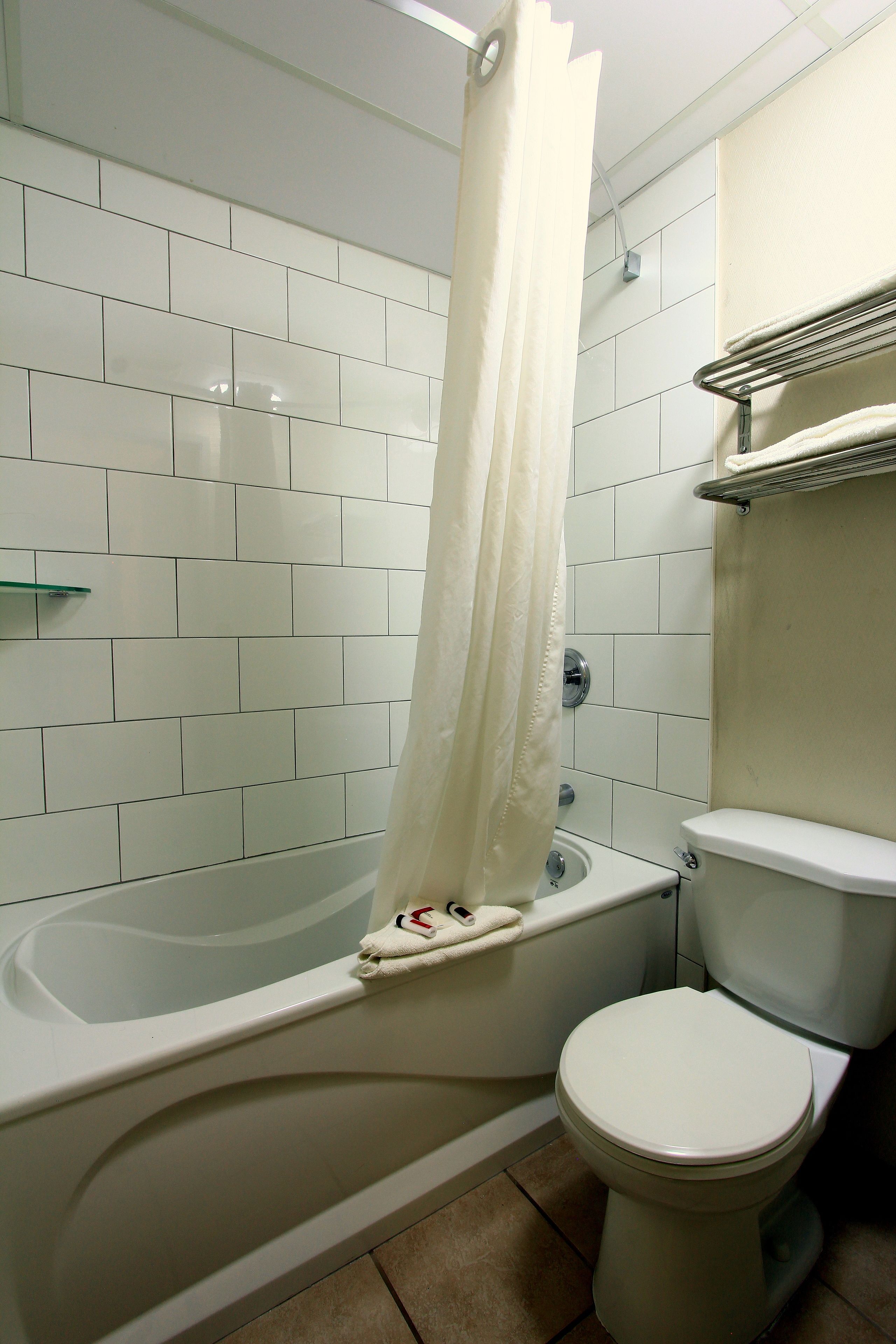 A bathroom with a bathtub, toilet, and a glass shelf.