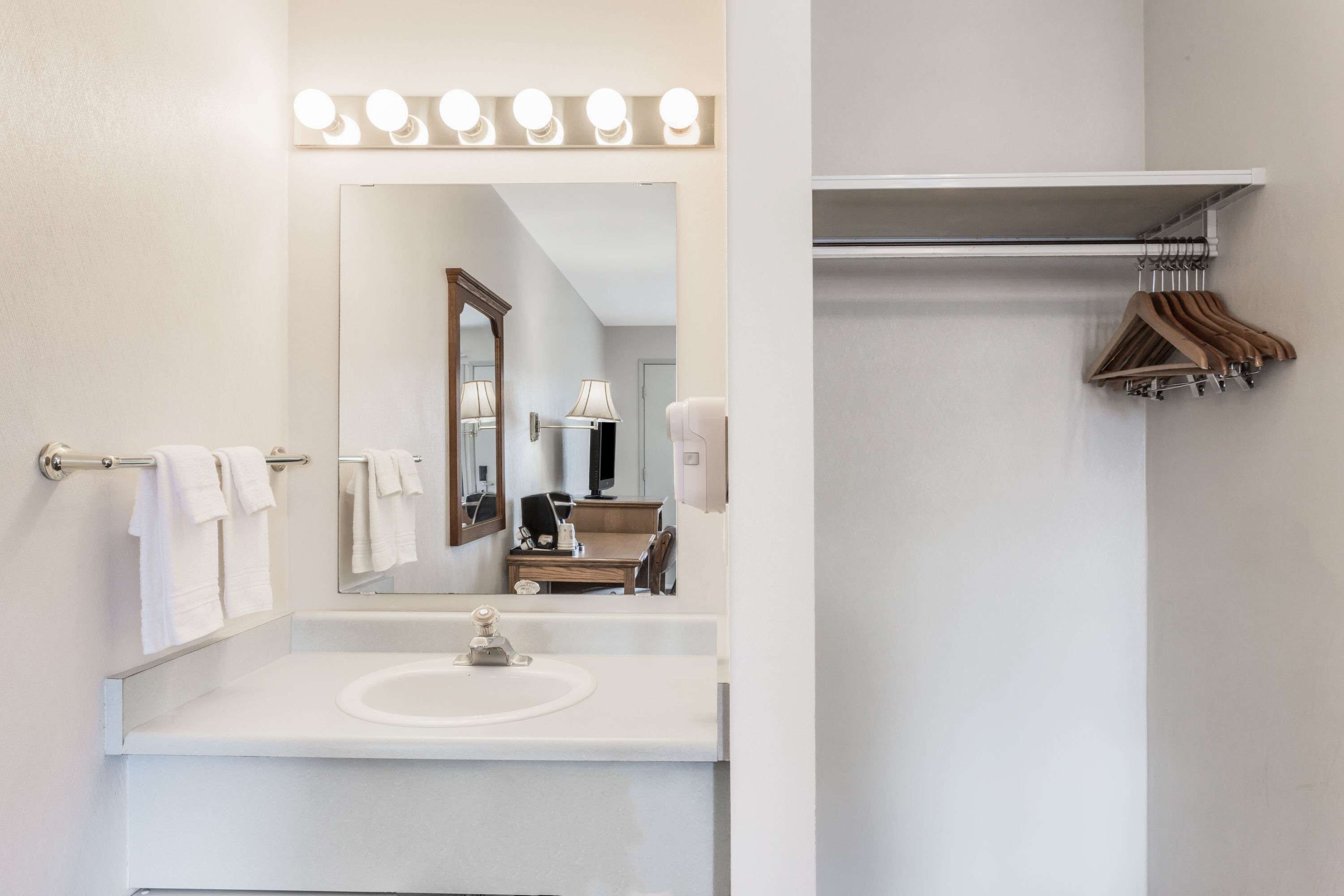 Un baño con lavamanos blanco, espejo y toallero.
