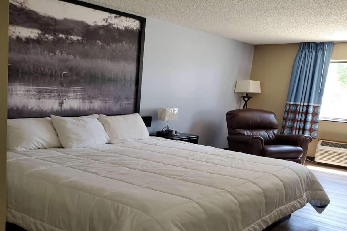 Una cama grande con cubrecama acolchado, una mesita de noche con lámpara, un sillón de cuero y una obra de arte colgada en la pared.