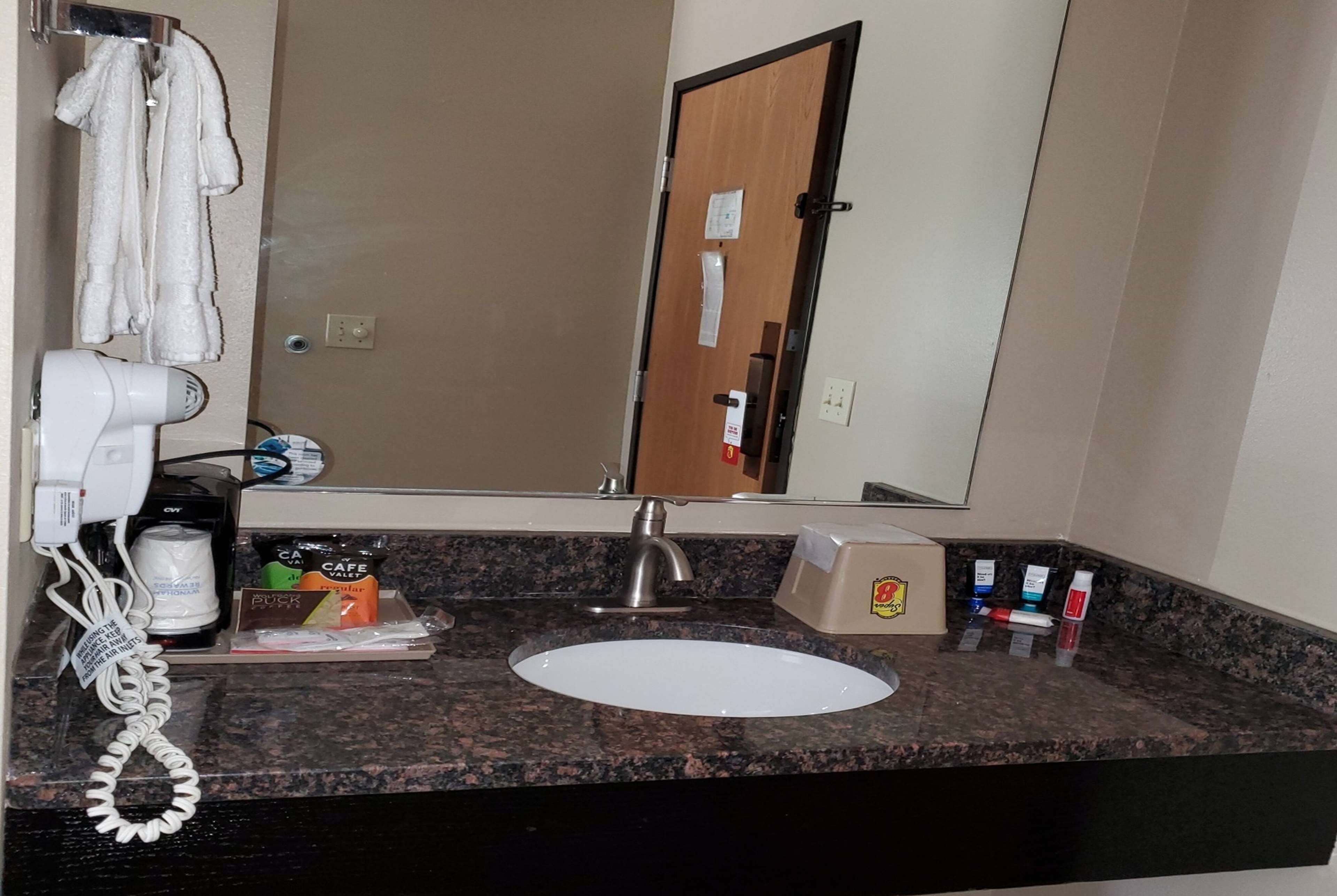 Un baño con lavamanos, secador de pelo, espejo y artículos de aseo en la encimera.
