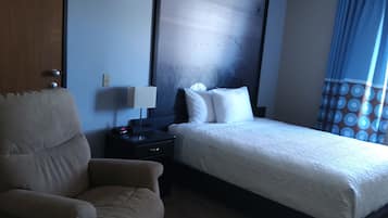A hotel room with a bed, a chair, a nightstand, and a wall with a large abstract painting.