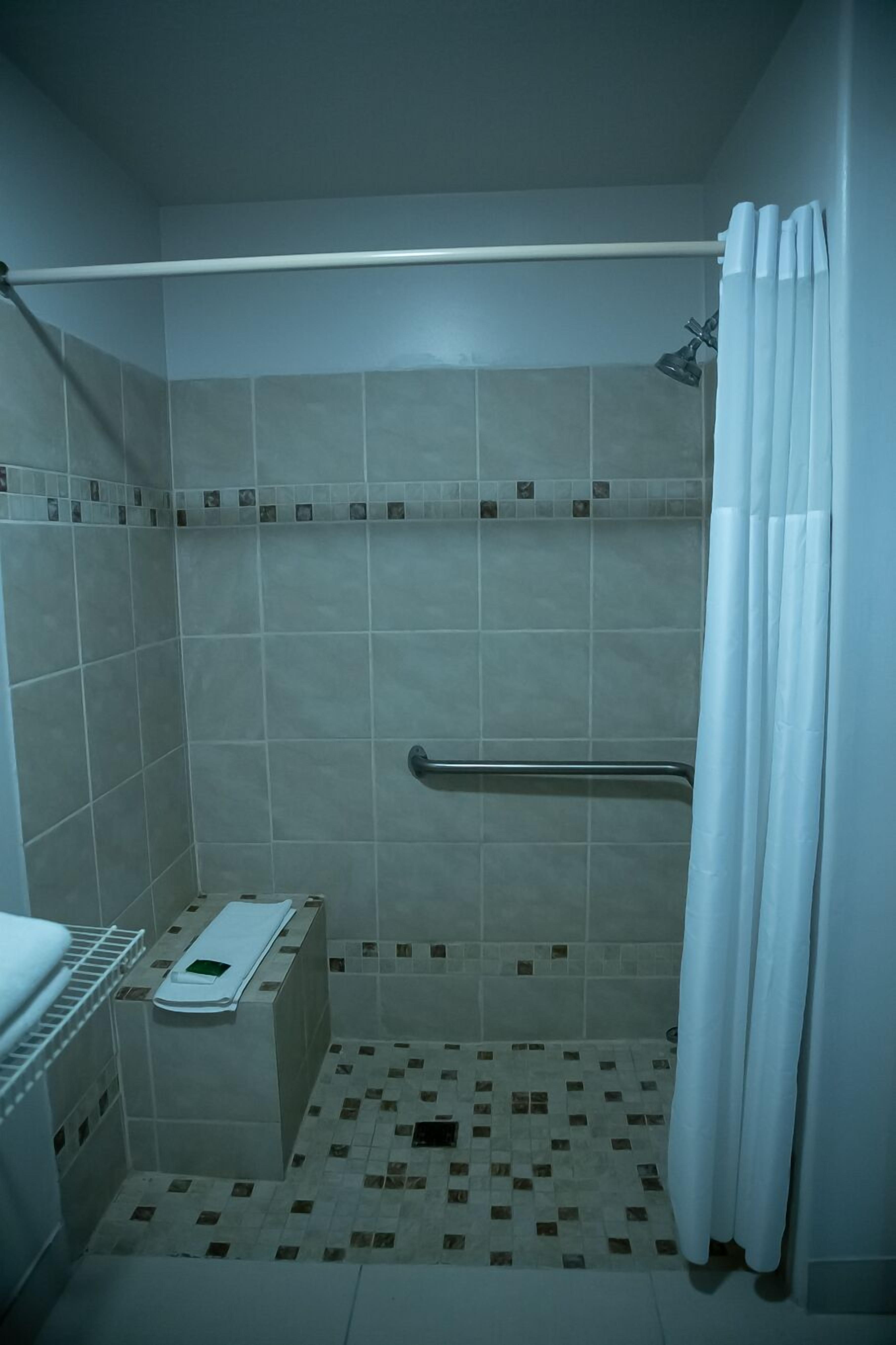 A small, tiled shower area with a handrail, a shelf with a towel, and a shower curtain.