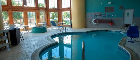 An indoor swimming pool with clear glass walls, wooden beams, and a tiled floor.