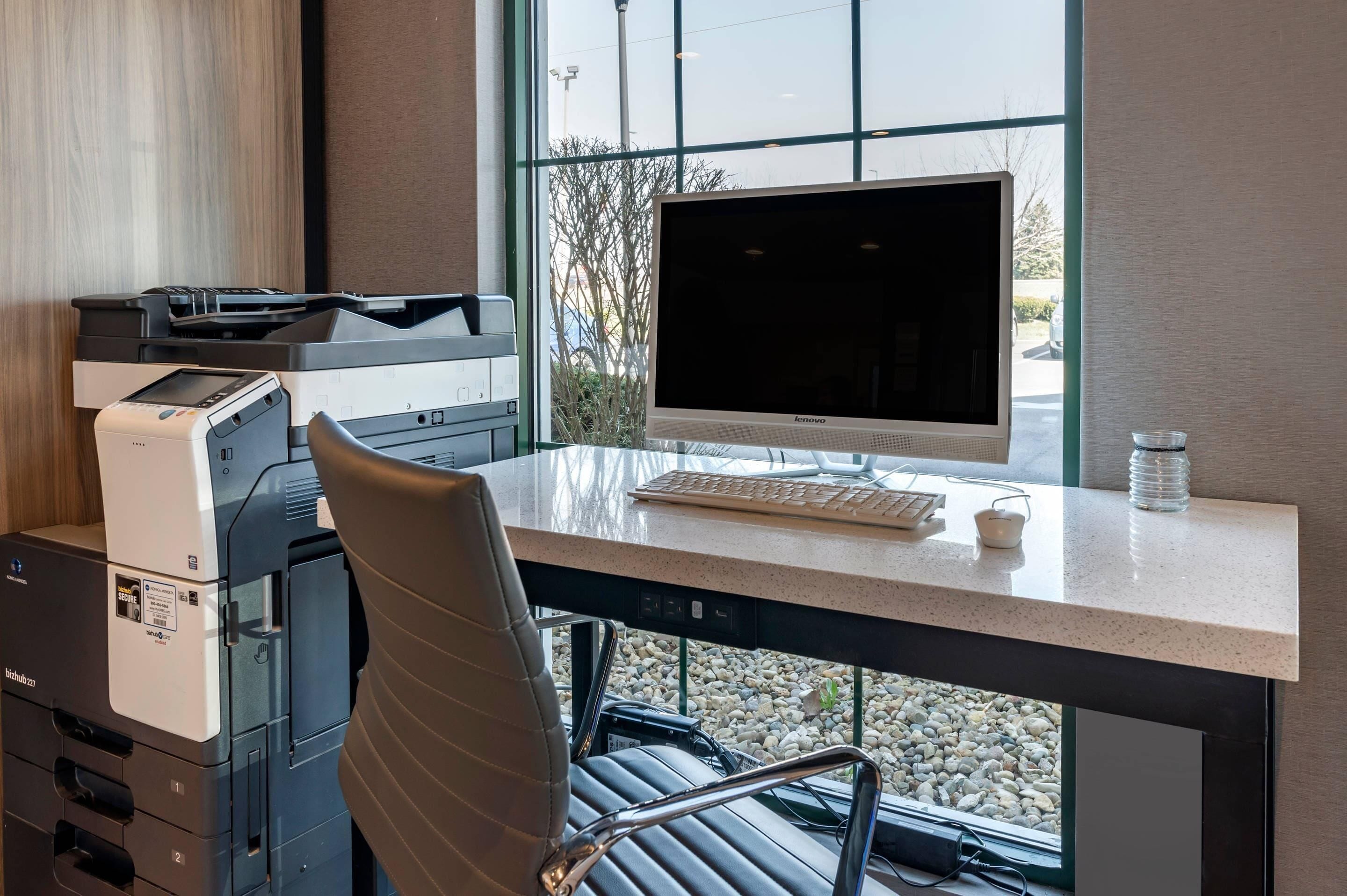 Un espacio de oficina moderno con un escritorio grande, una computadora de escritorio, una impresora y una silla.