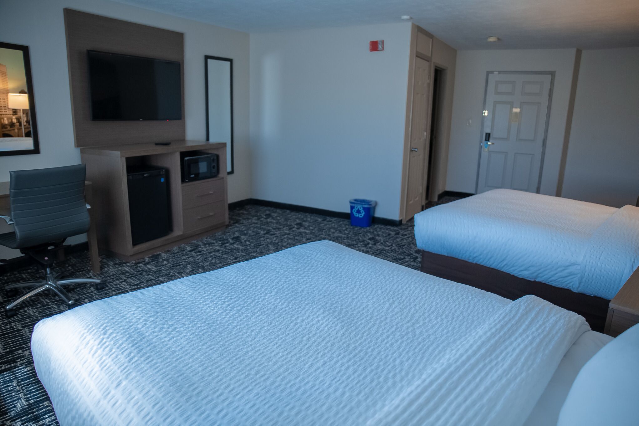Habitación de hotel con dos camas, un escritorio con computadora, televisión y un pequeño cubo de basura.