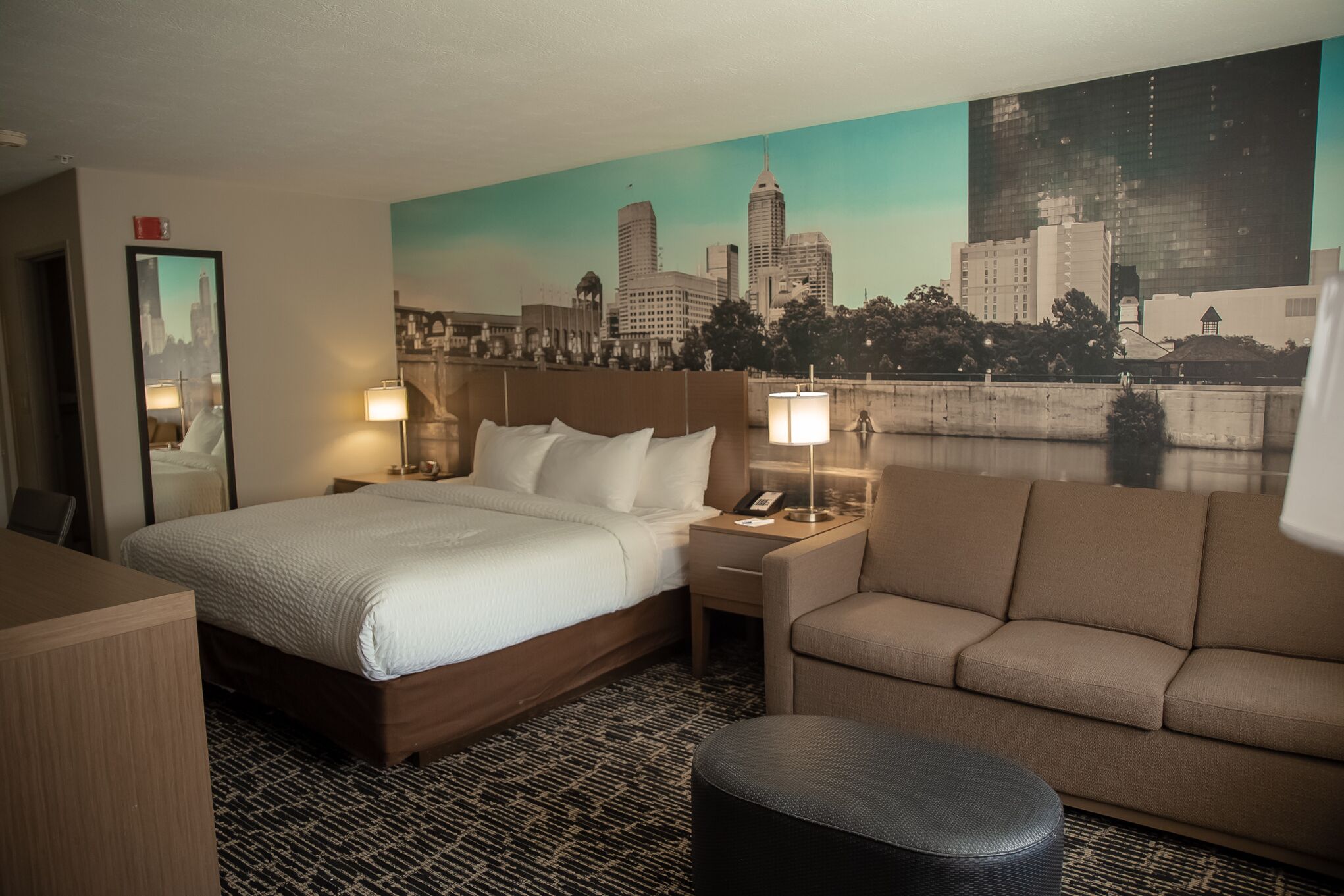 Een hotelkamer met een bed, een slaapbank, een bureau en een stadsgezicht muurschildering.
