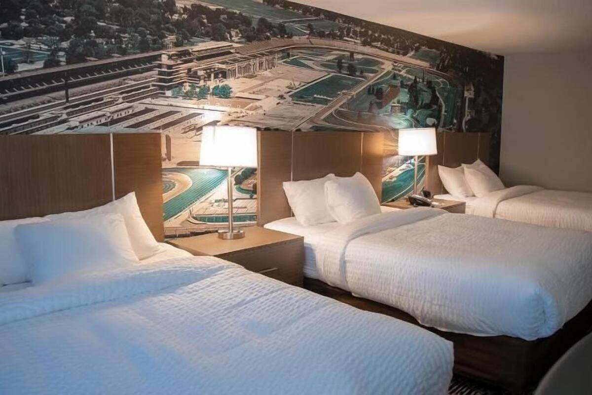 A hotel room with two beds, a large mural on the wall, and a view of a cityscape.