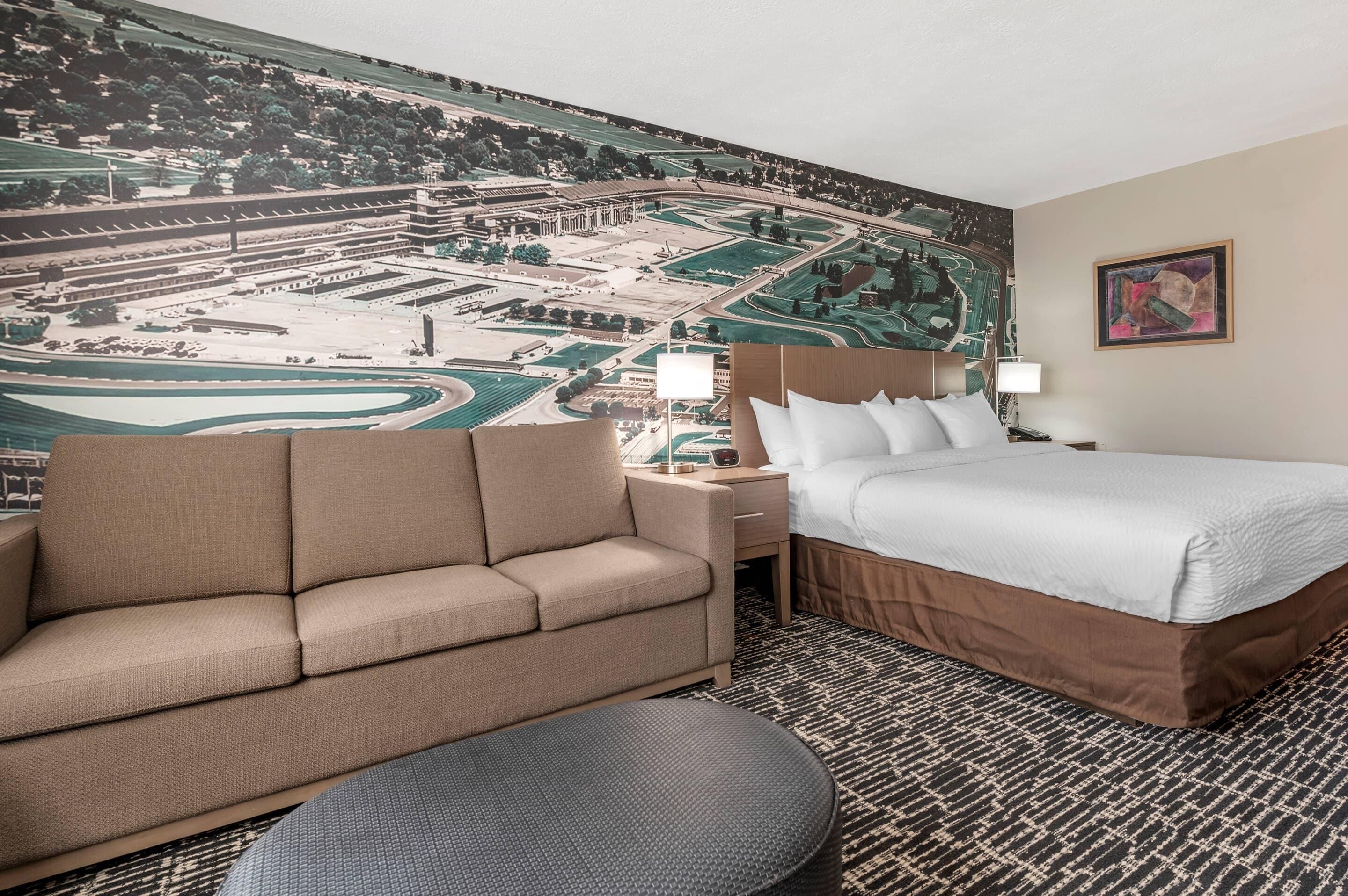 A hotel room with a large bed, a sofa, a small table, and a wall mural of a landscape.