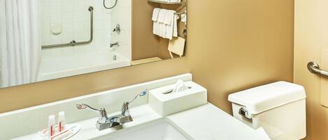 Un baño con lavamanos blanco, espejo, toallero y retrete.