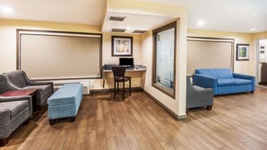 Een hotelkamer met een houten vloer, een bureau met een computer, een blauwe fauteuil, een grijze fauteuil en een blauwe bank.