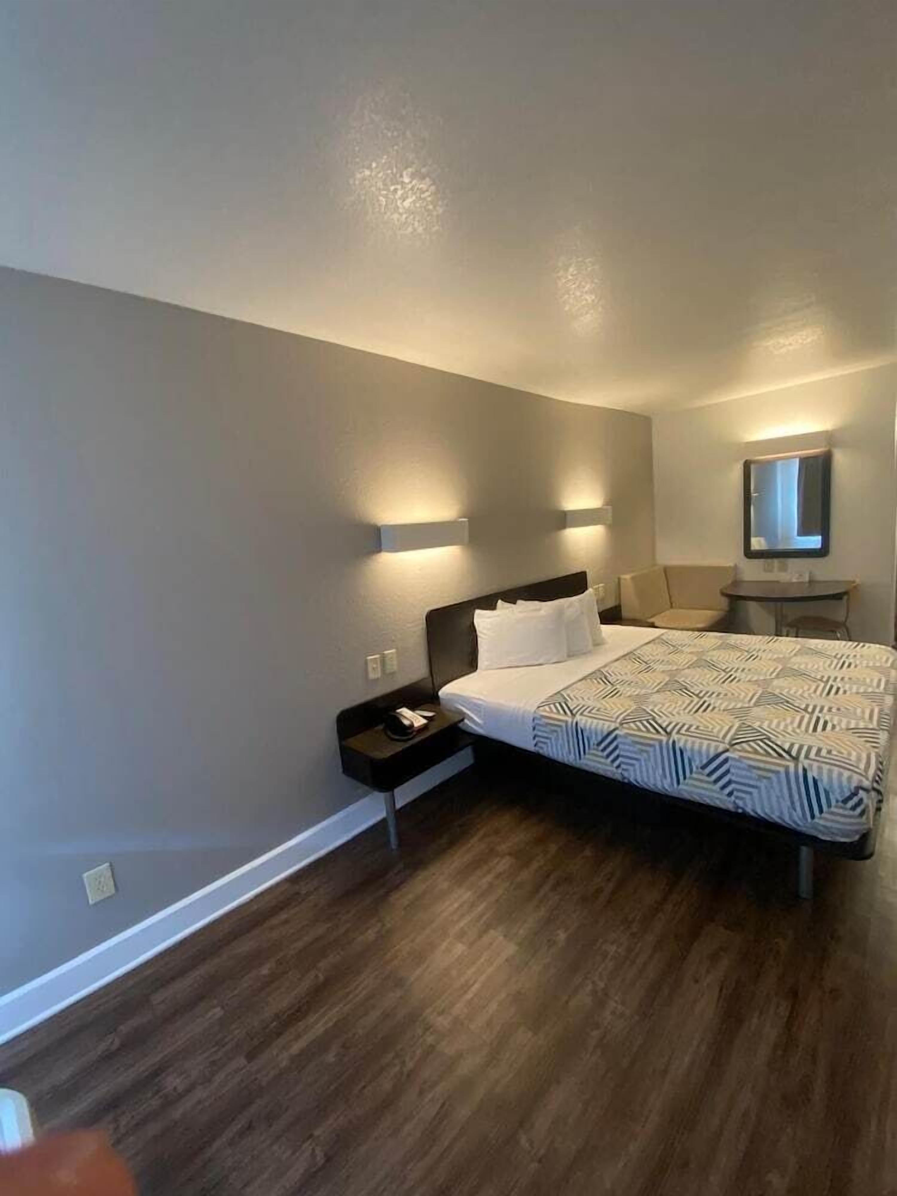 A modern bedroom with a large bed, bedside tables, a nightstand, a mirror, and wall-mounted lighting.