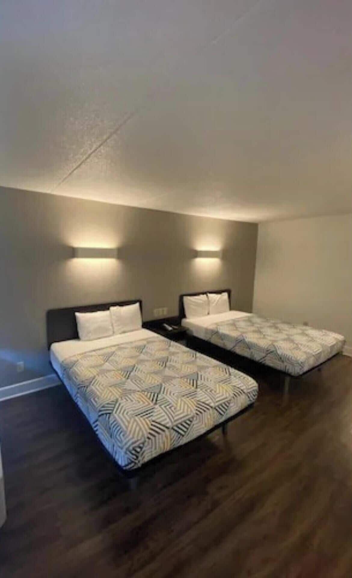 A room with two beds, each with patterned bedding and headboards, and wall-mounted lighting.