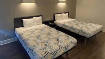A room with two beds, each with patterned bedding and headboards, and wall-mounted lighting.