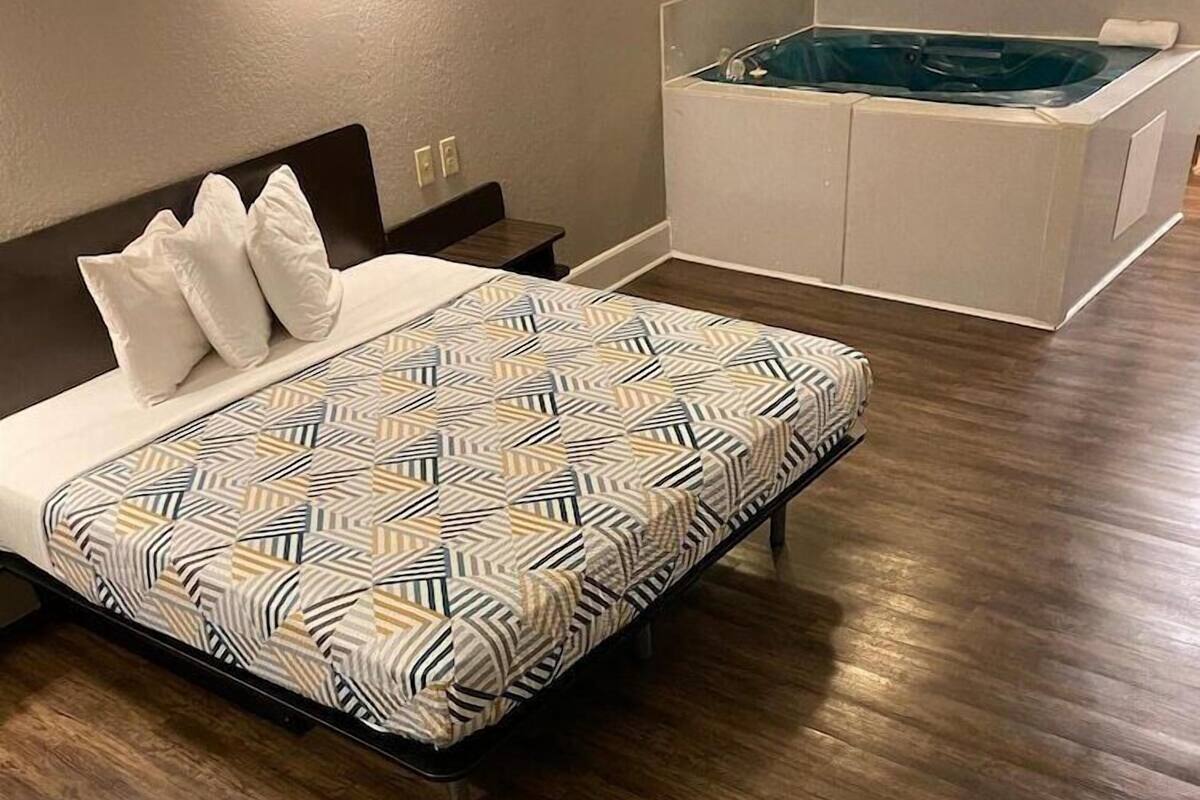 A modern bedroom with a bed, a wooden floor, and a separate bathroom with a bathtub.