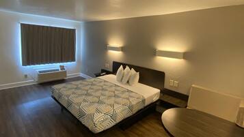 A hotel room with a bed, bedside table, chair, and a window with curtains.