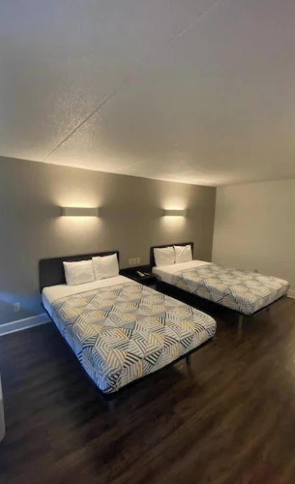 Une chambre avec deux lits, chacun recouvert d’une couvre-lit à motifs, et deux appliques murales.