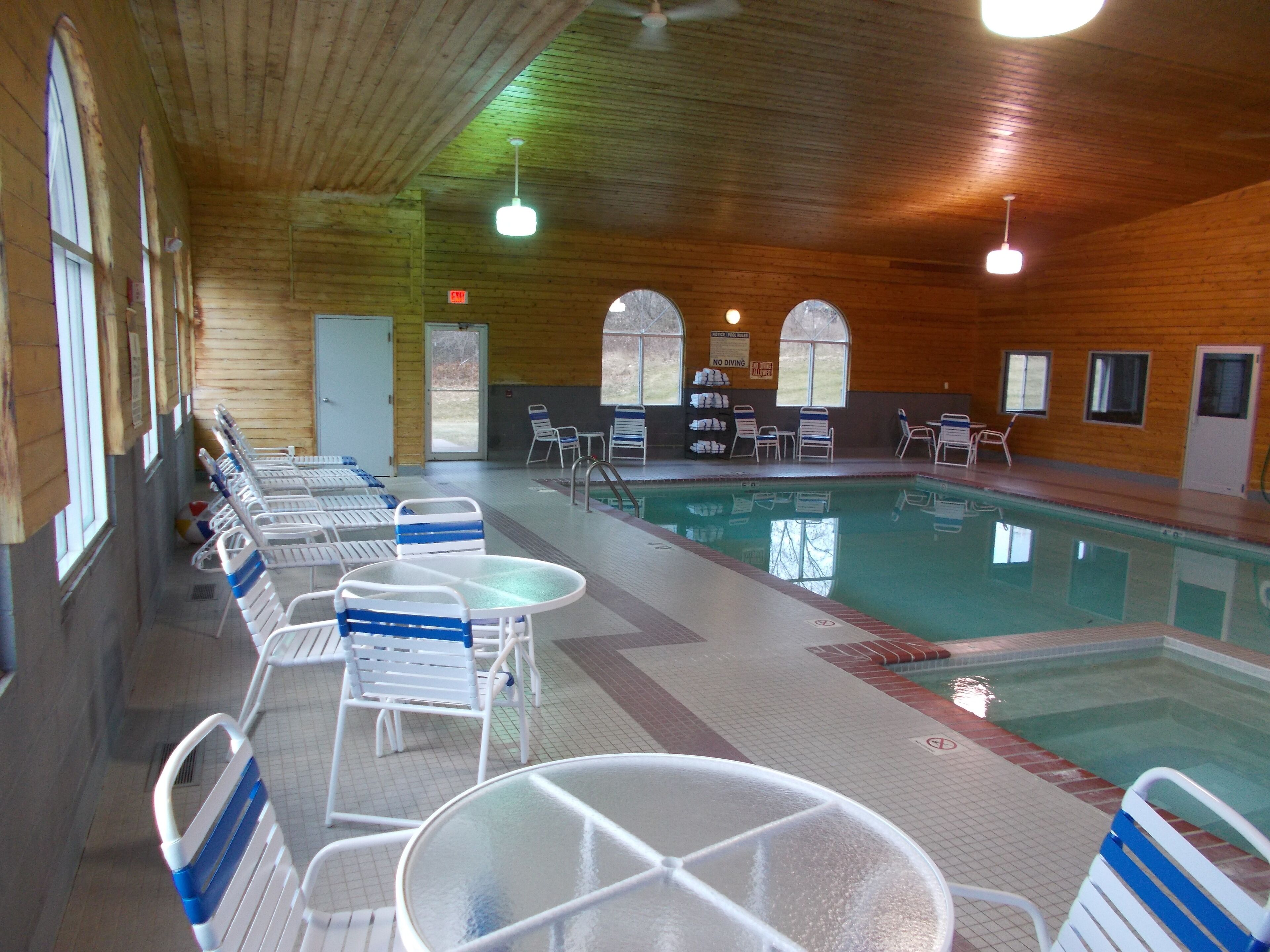 An indoor swimming pool with multiple lanes, lounge chairs, and tables arranged around the pool area.