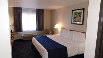 Hotelkamer met een bed, een bureau, een stoel, een raam met gordijnen, een wandlamp en een ingelijste foto.