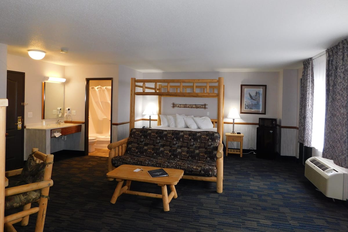 A hotel room with a bed, a desk, a chair, a bedside table, a lamp, and a mirror.
