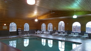 En inomhuspool med kristallklart vatten, omgiven av solstolar och bänkar, träväggar och stora, välvda fönster.