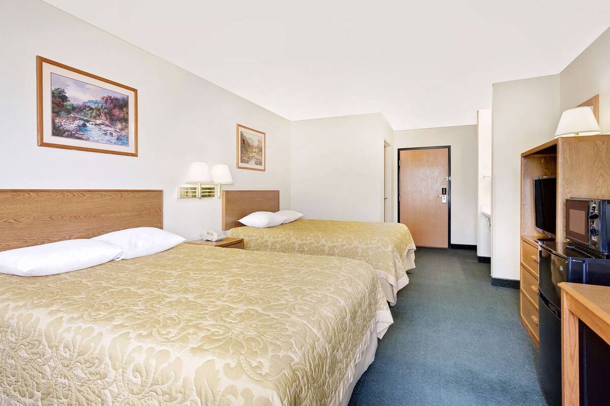 Een hotelkamer met twee bedden, een bureau met een televisie, en een deur naar een andere kamer.