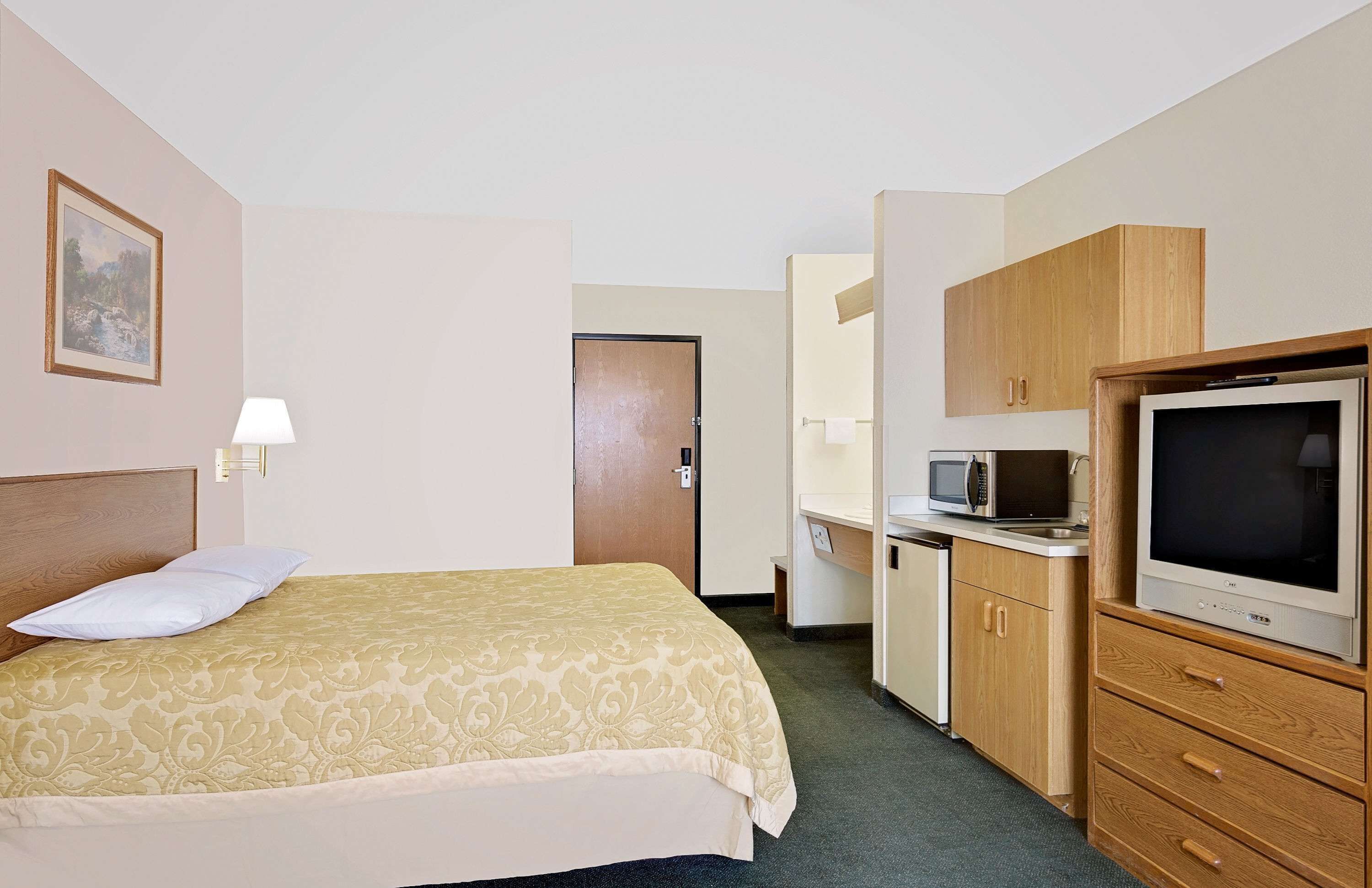 Una habitación de hotel con cama, televisor, microondas y una pequeña kitchenette.