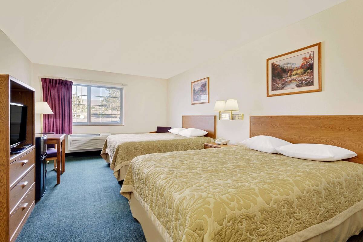 Een hotelkamer met twee bedden, een bureau, een televisie en een raam met gordijnen.
