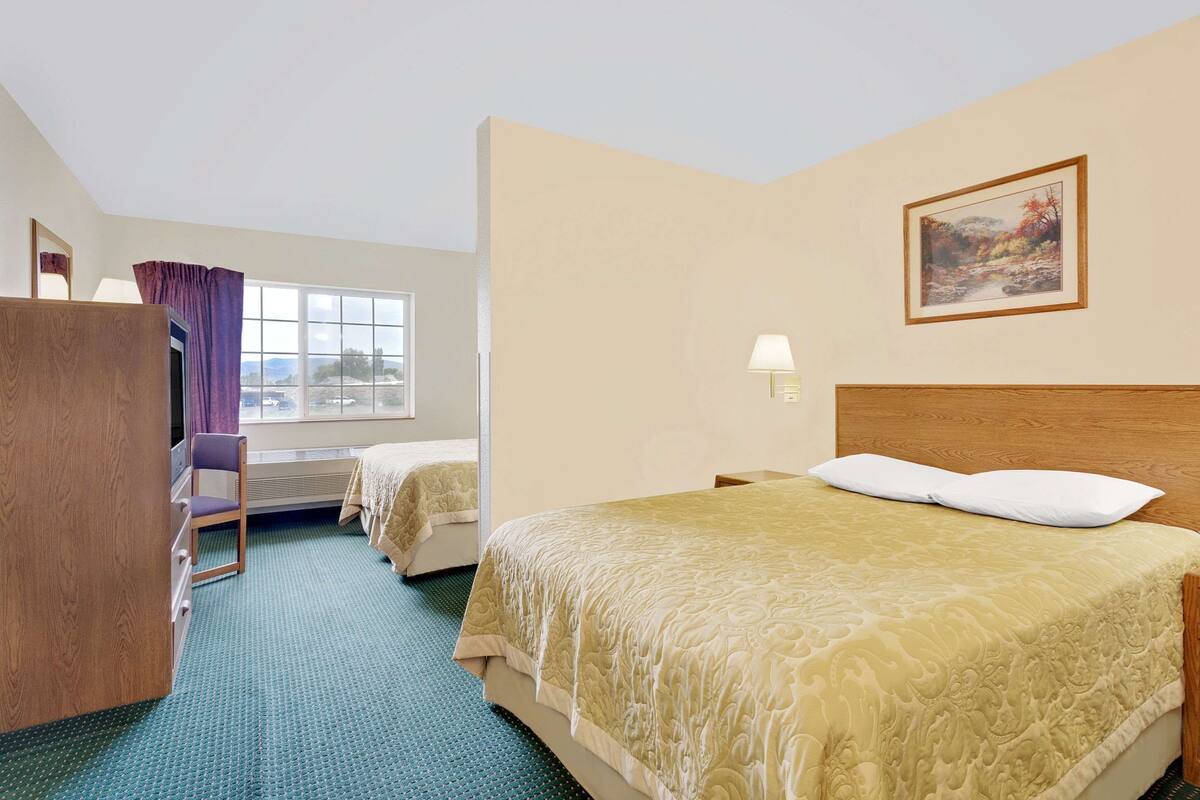 Een hotelkamer met een groot bed, een bureau, een stoel, een raam met gordijnen en een schilderij aan de muur.