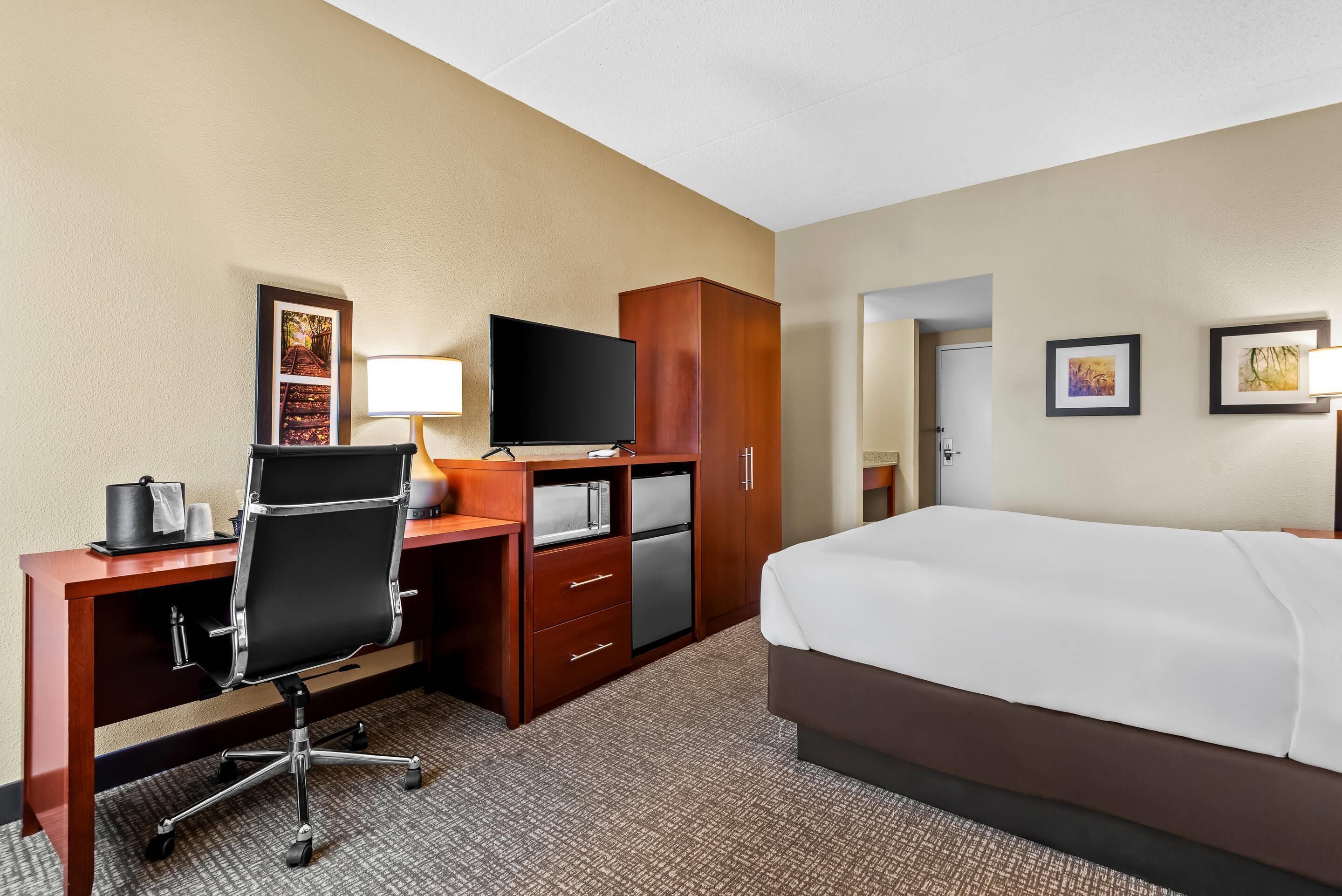 A hotel room with a bed, desk, chair, television, and wardrobe.