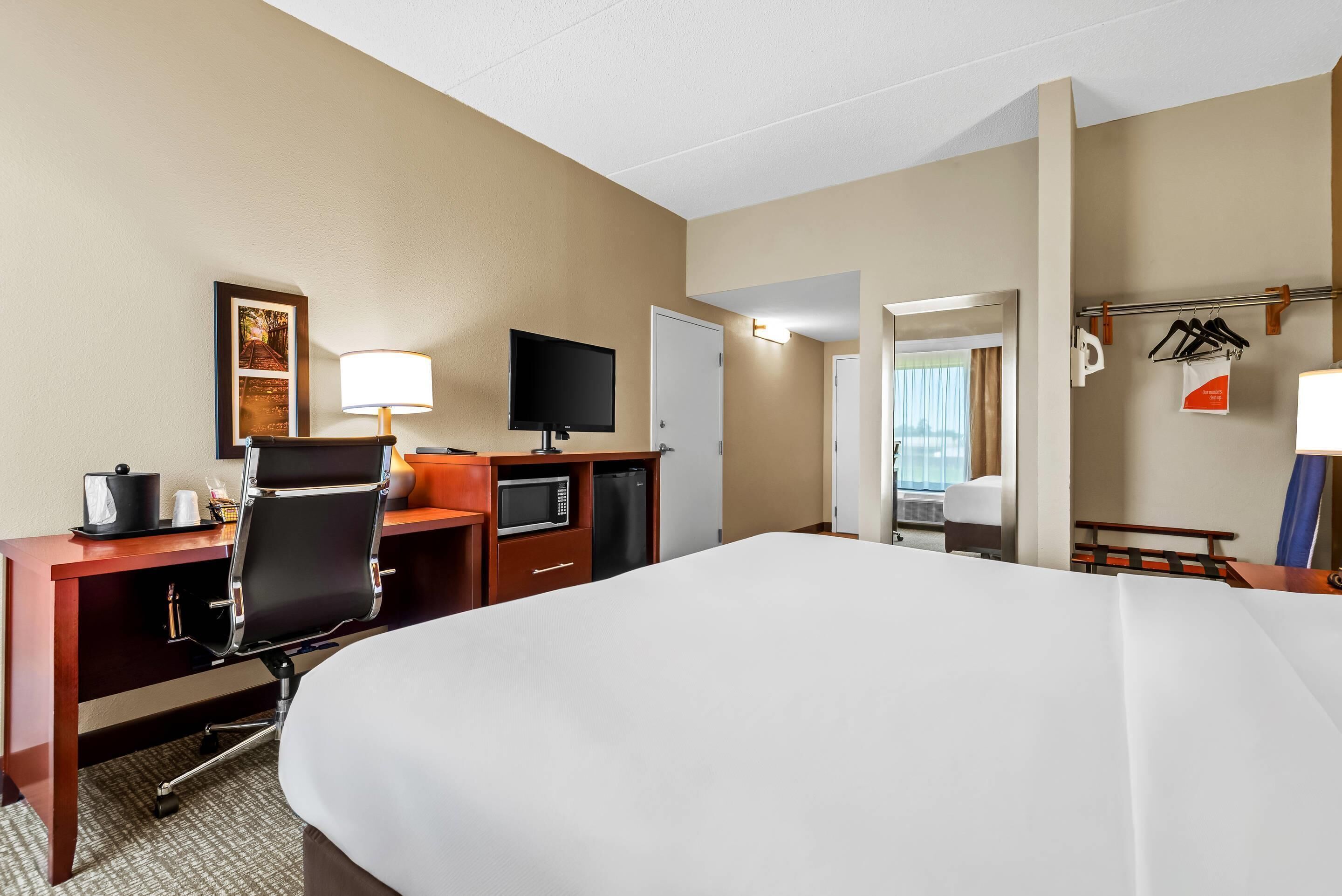 A hotel room with a large bed, a desk with a computer, a TV, and a microwave.