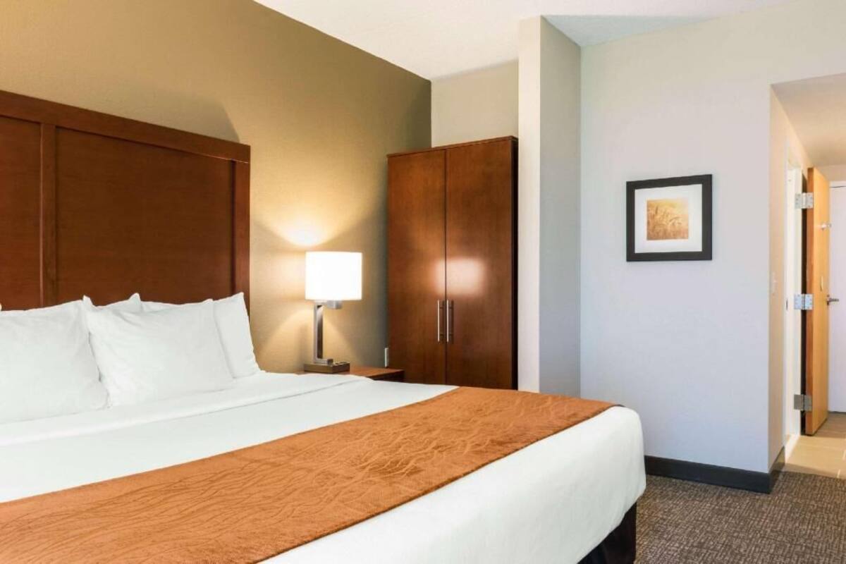 Une chambre d’hôtel avec un lit, une table de chevet, une lampe, une armoire et une porte.