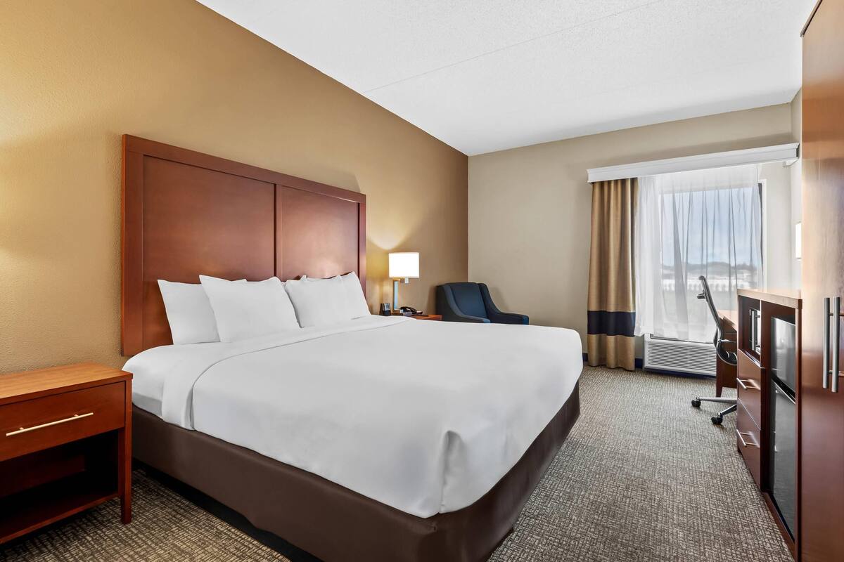 Une chambre d’hôtel avec un grand lit, un bureau, une chaise, une lampe de bureau et une vue sur l’extérieur par une fenêtre.