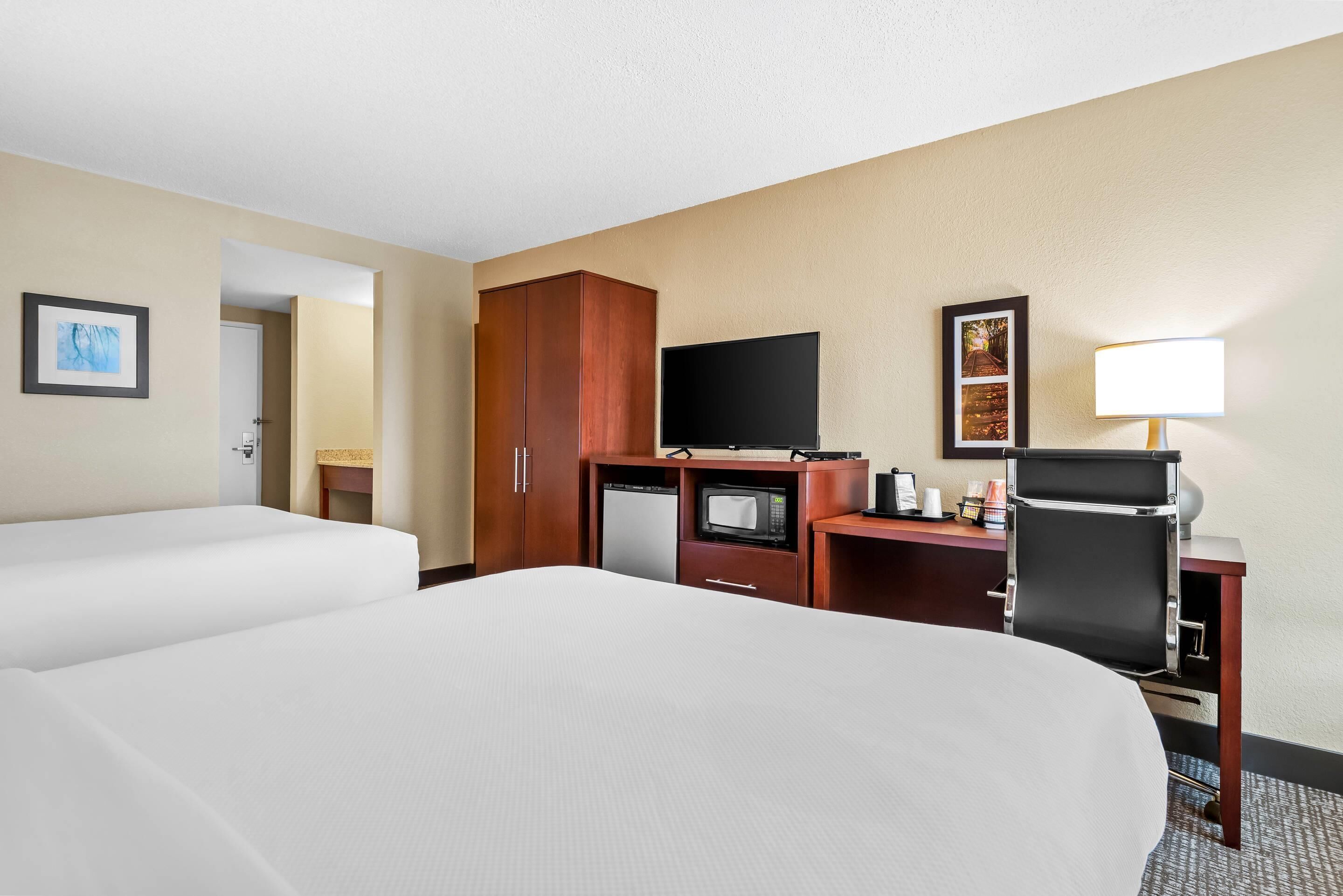 Een hotelkamer met twee bedden, een bureau met een computer, een televisie, een magnetron en een lamp.