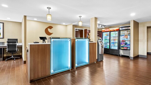 A reception area with a wooden desk, a blue glass partition, a vending machine, and a refrigerator. - Comfort Inn Chambersburg North (Chambersburg)