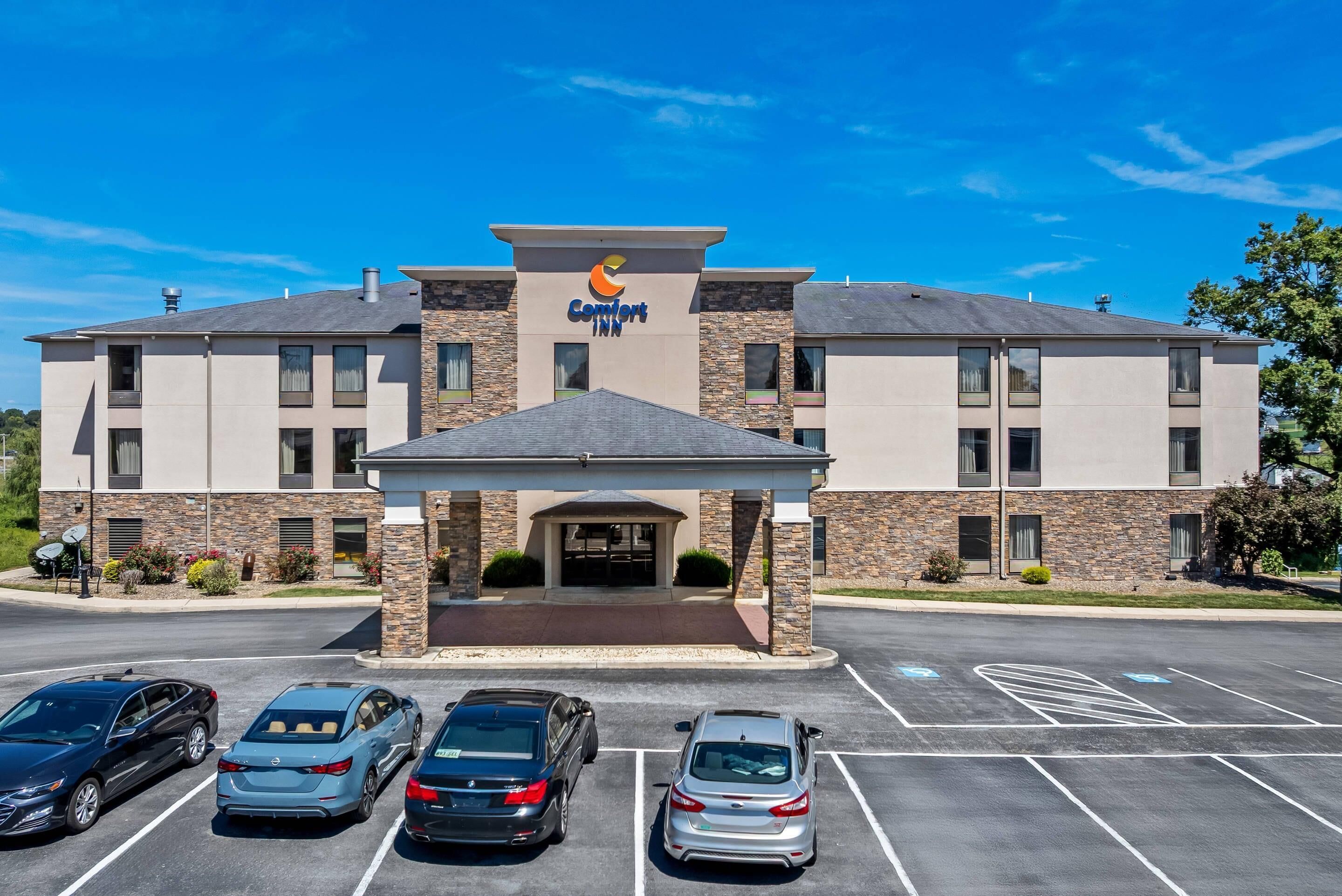 A Comfort Inn hotel with a modern design, featuring a stone facade, a covered entrance, and a parking lot with several cars.