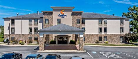 A Comfort Inn hotel with a modern design, featuring a stone facade, a covered entrance, and a parking lot with several cars.