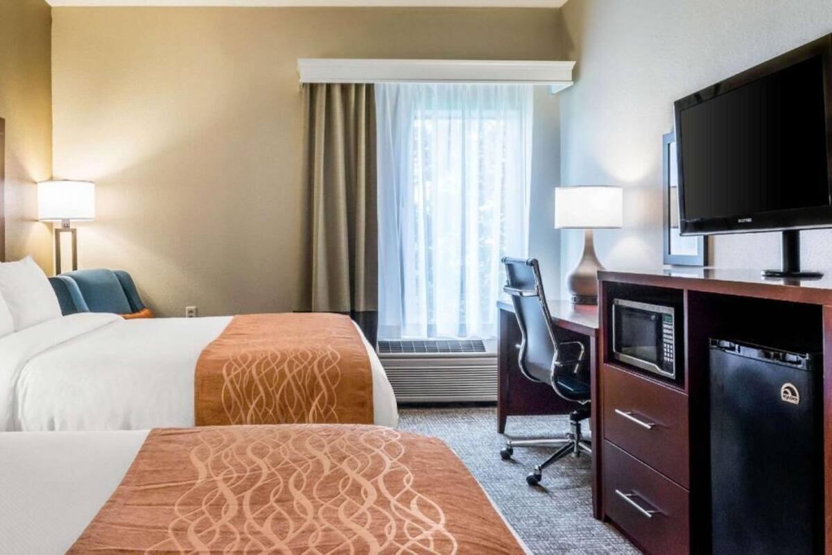Une chambre d’hôtel avec deux lits, un bureau avec une chaise, une télévision, un four à micro-ondes et un réfrigérateur.