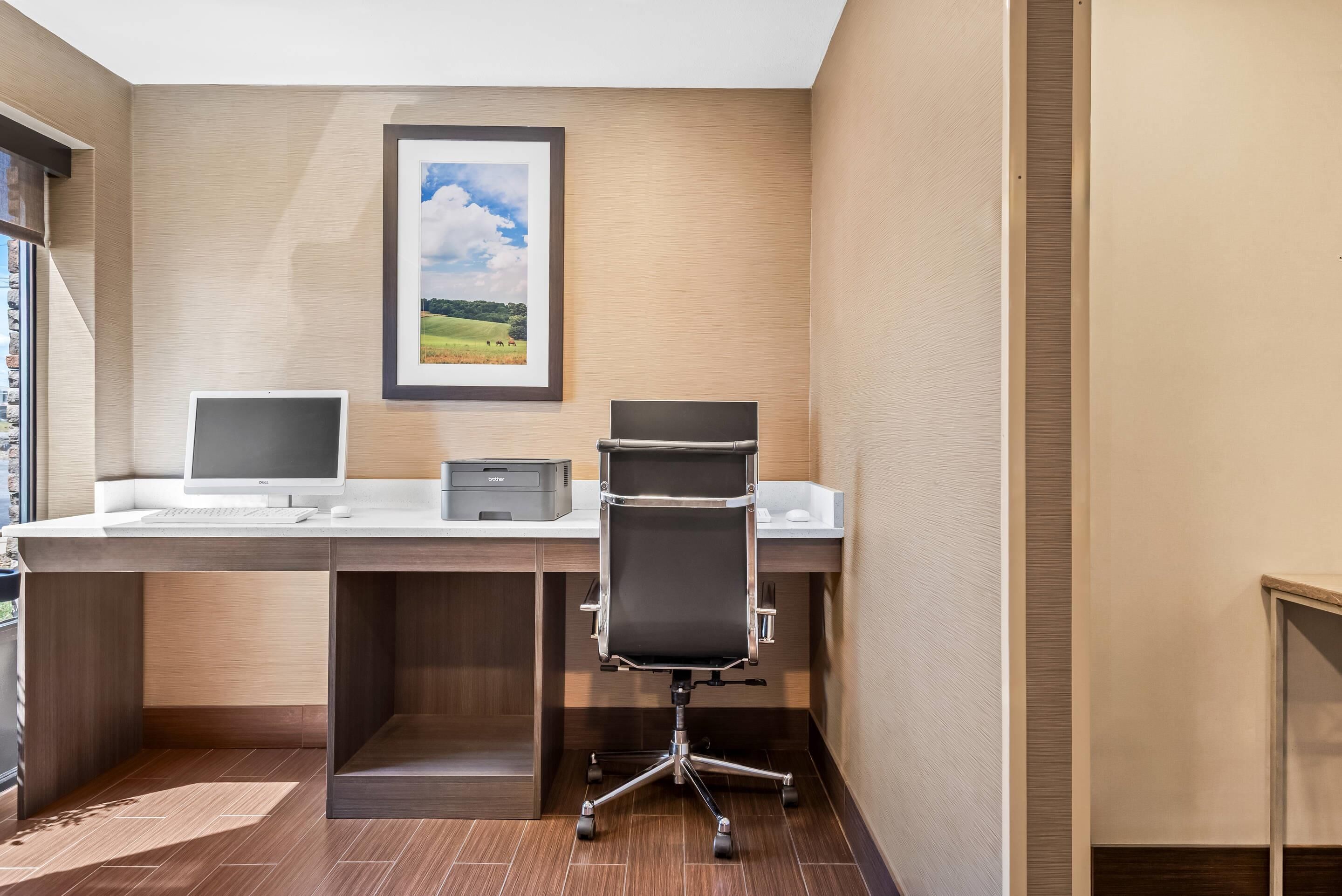 A hotel office with a desk, two monitors, a printer, and a chair.