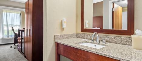 A hotel bathroom with a granite countertop sink, wooden vanity, and a large mirror.