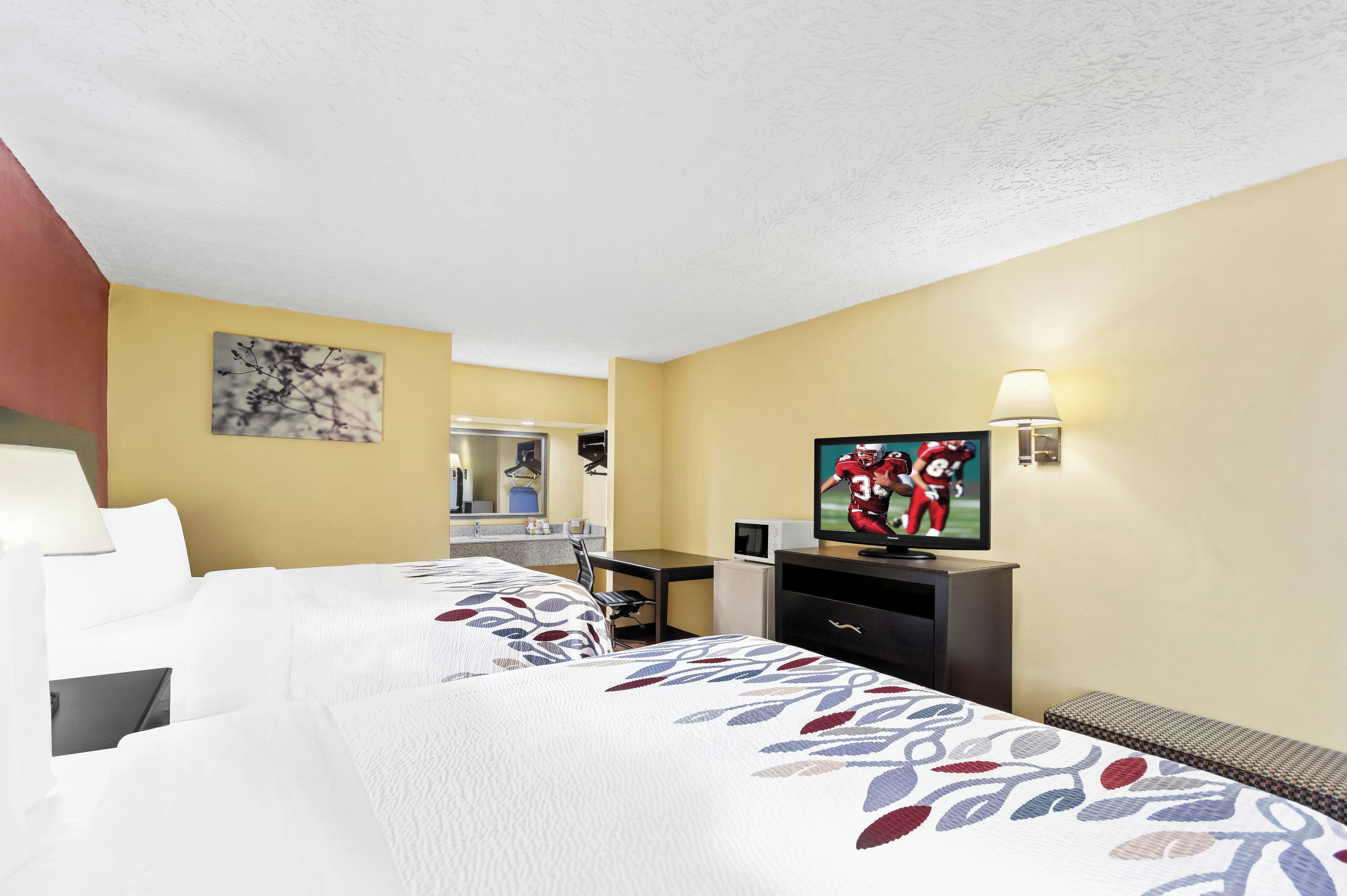 A hotel room with two beds, a desk, a television, and a mirror.