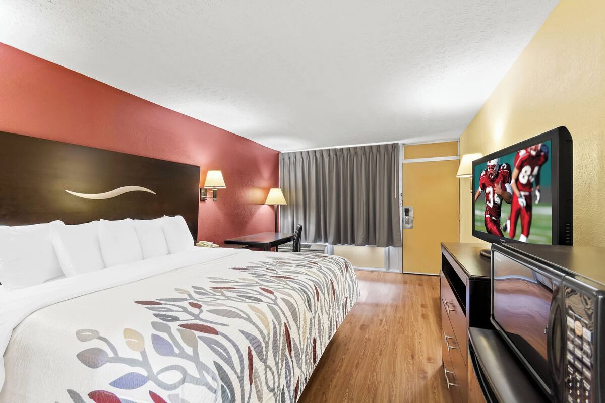 A hotel room with a bed, a TV, a desk, and a lamp.