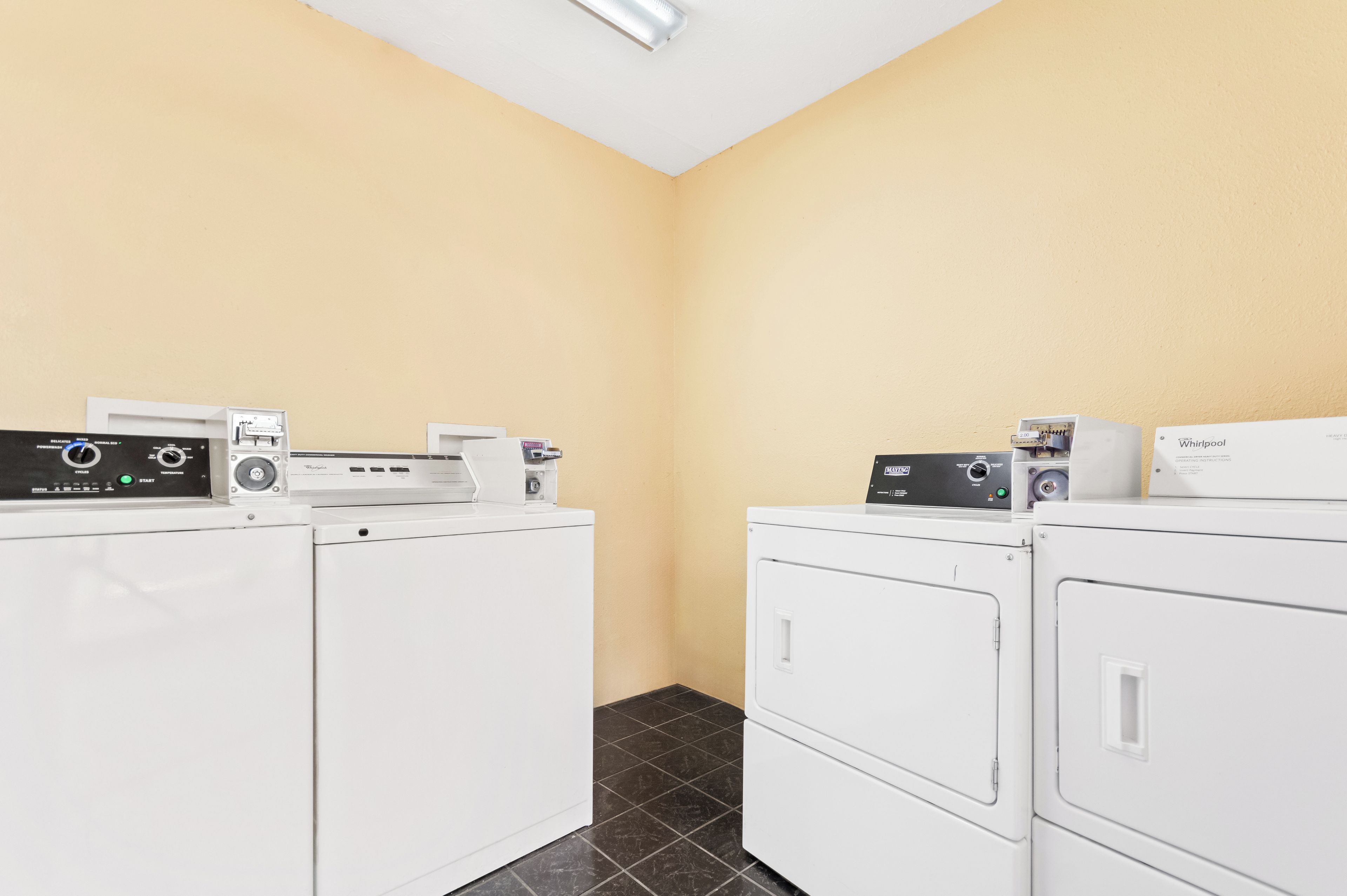 A laundry room with two stacked washers and dryers, control panels, and a wall-mounted light fixture.
