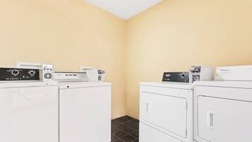A laundry room with two stacked washers and dryers, control panels, and a wall-mounted light fixture.