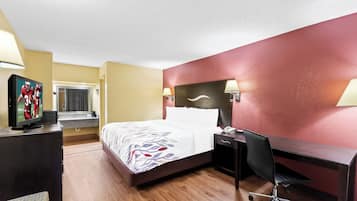 A hotel room with a bed, desk, chair, TV, and lamps.