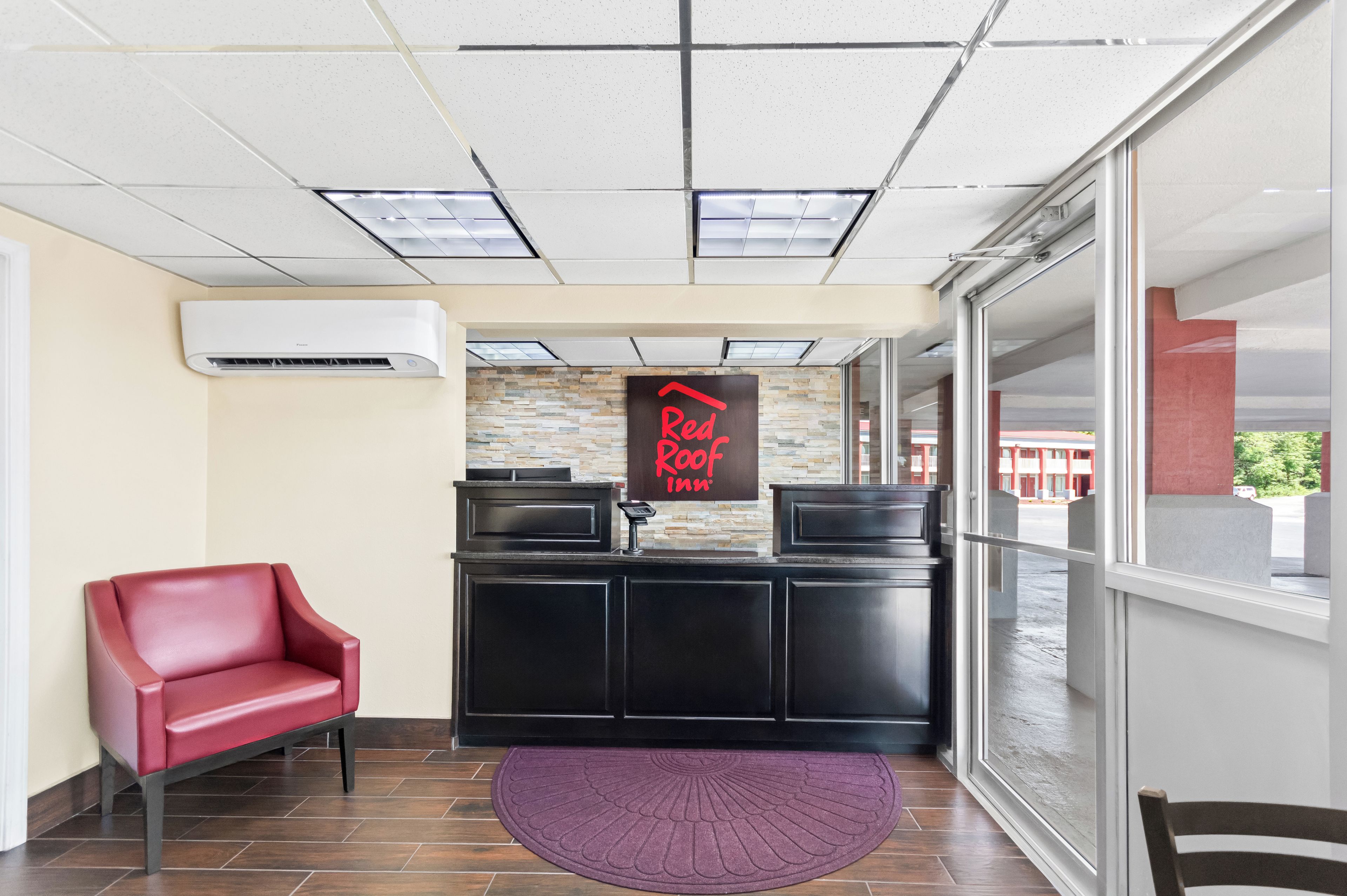 A reception area with a red leather chair, a black reception desk, and a Red Roof Inn sign.